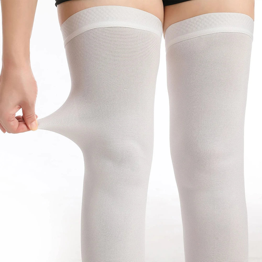 A close-up of a pair of light gray medical-grade compression stockings being worn on a leg.