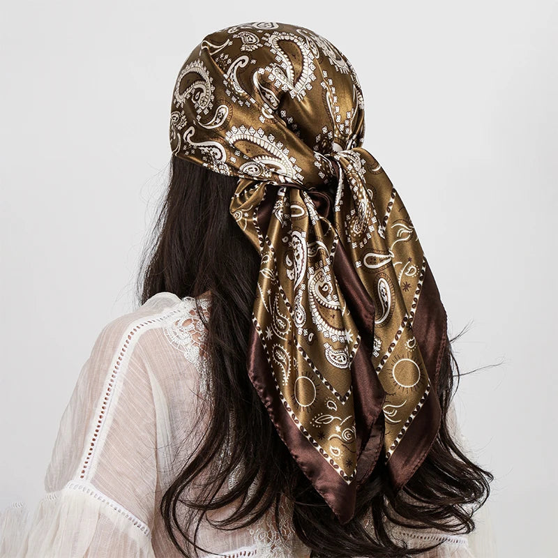 A woman with long dark hair is wearing a brown and gold paisley silk shawl scarf tied around her neck.