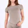 A woman wearing a fitted, short-sleeve performance fitness top in a taupe color.