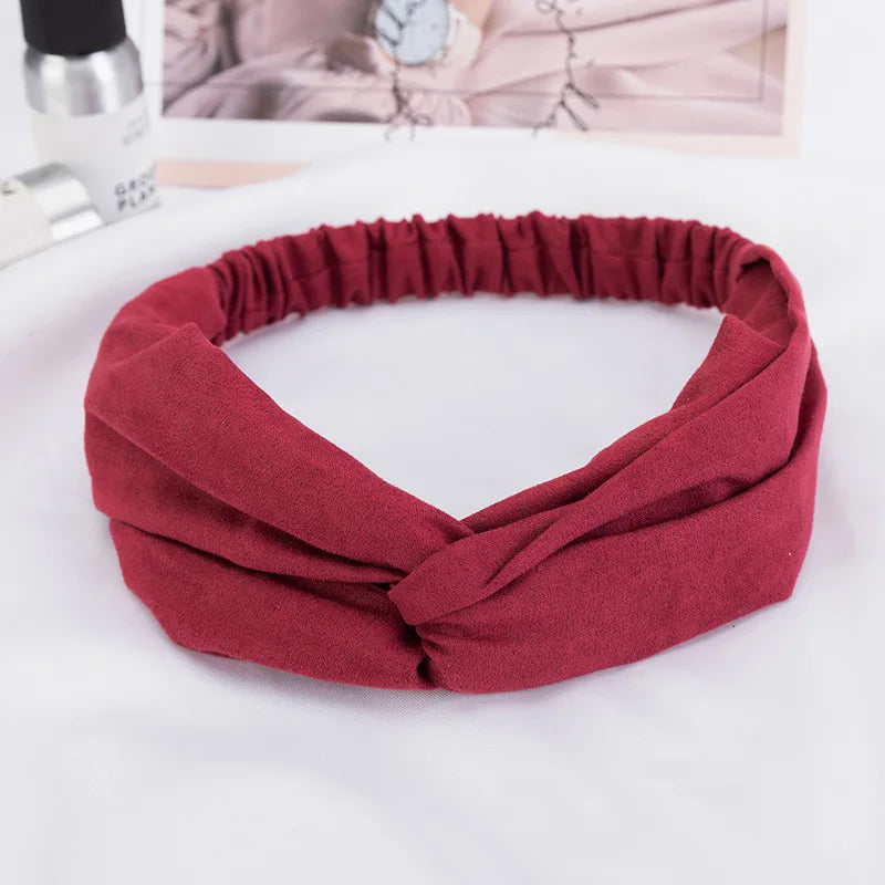 A maroon fabric headband or hair accessory is shown lying on a white surface.