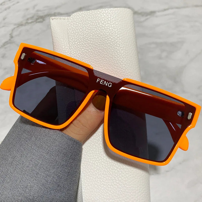 Orange-framed square sunglasses resting on a white textured surface.