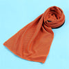 Orange microfiber cooling towel rolled up on a light blue background.