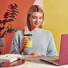 Una mujer joven sonriendo mientras usa un set de licuadora Magic Bullet de 11 piezas en una computadora portátil.