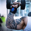 Un bras musclé avec des tatouages noirs et gris soulève une barre, démontrant des écarteurs de poignet pour l'entraînement en