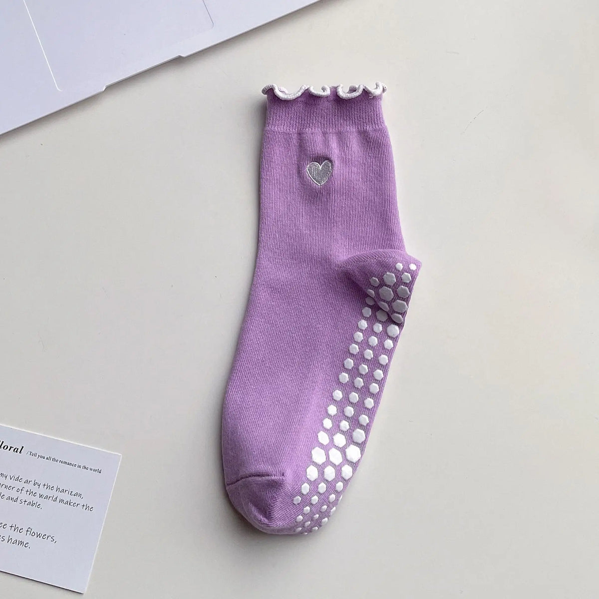 A purple yoga sock with a heart embroidery and silver dots on the toe, displayed on a white surface.
