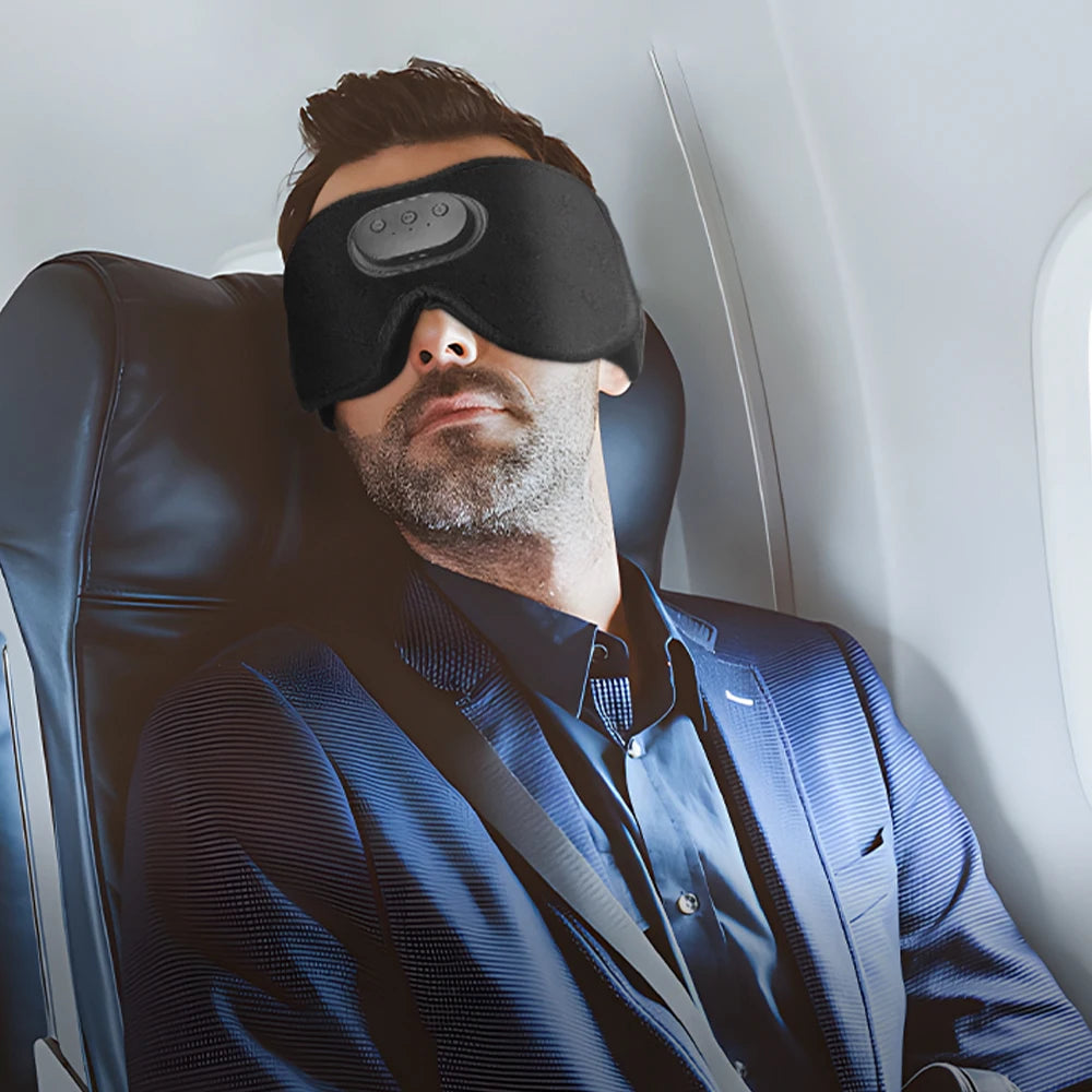 A man wearing a black sleep headphone mask is seated in a leather chair.