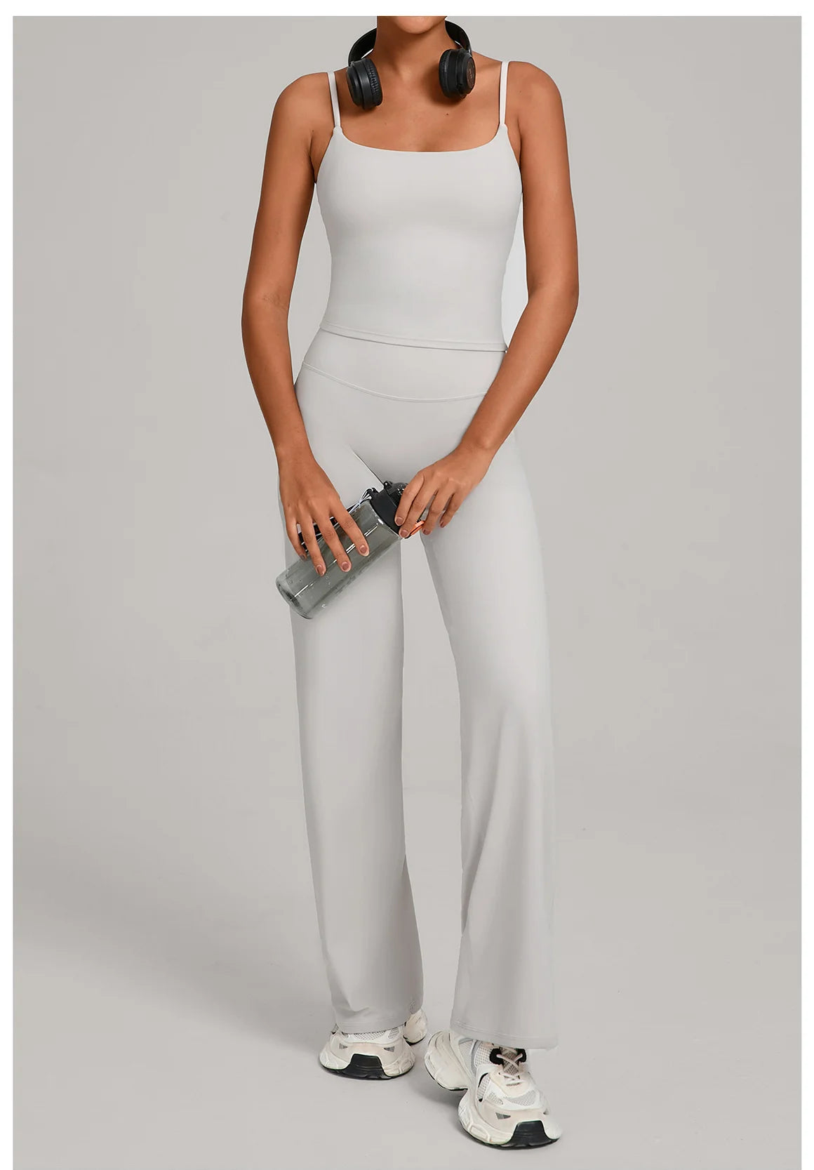 A woman models a light gray high-waist yoga and fitness tracksuit set with black headphones.