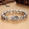A silver mantra charm bracelet with interlocking links and a round charm on a light brown surface.