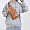 A man wearing a gray hoodie and jeans holds a brown leather crossbody bag.