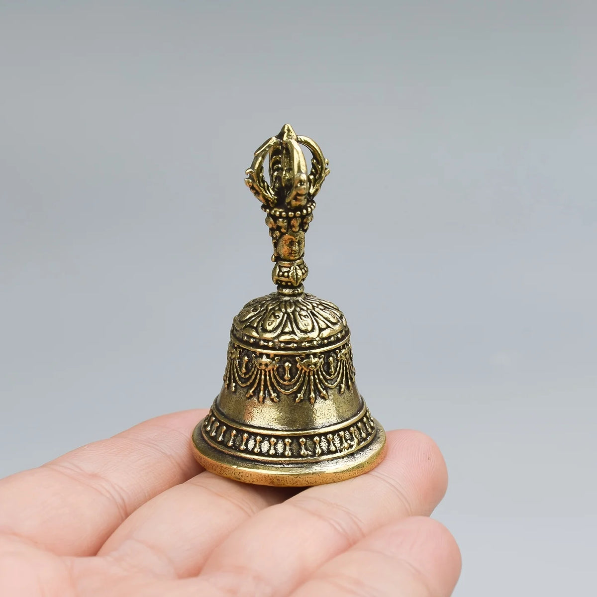 Une main tient une petite cloche à secouer en bronze antique avec un dessus orné et une base évasée.