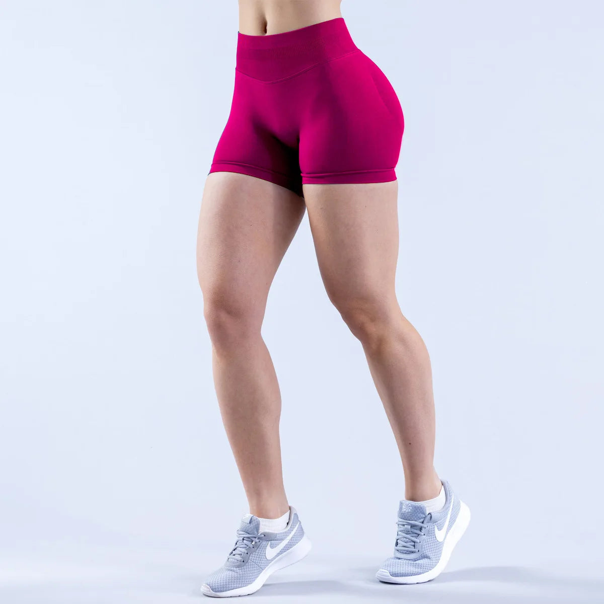 A person wearing magenta seamless high-waisted yoga shorts and light gray athletic shoes.