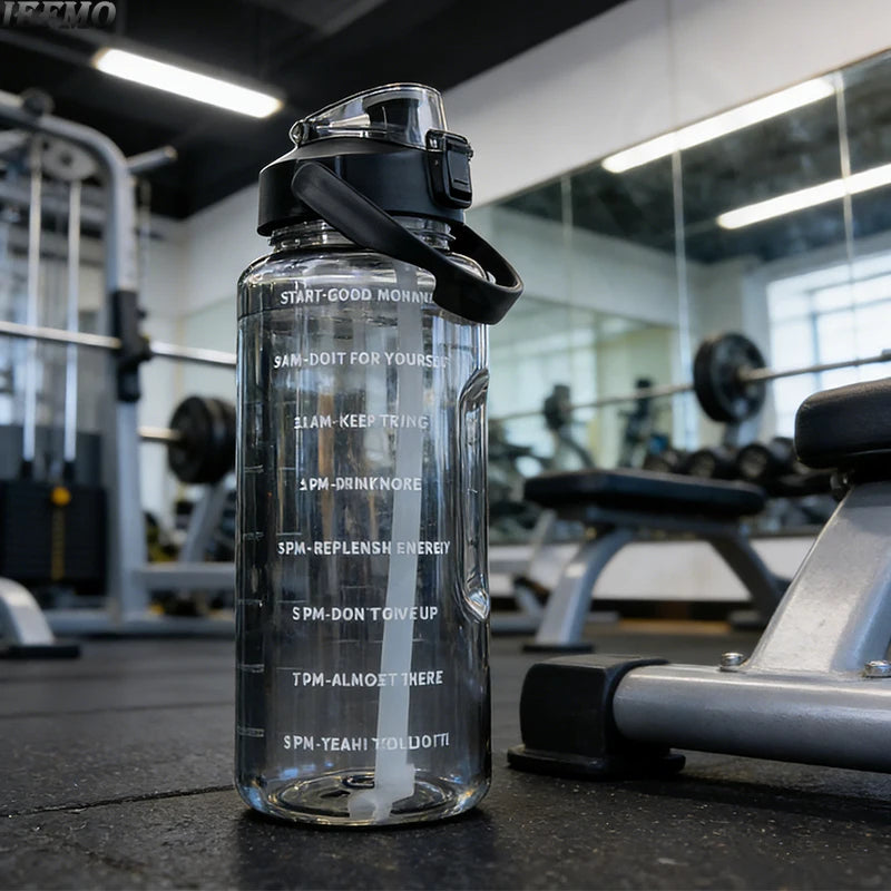 Klare Wasserflasche mit schwarzem Deckel und Zeitmarkierungen auf einem dunklen Fitnessboden.