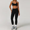 A woman wearing a black three-piece yoga sports set consisting of a sports bra, sports top, and leggings.