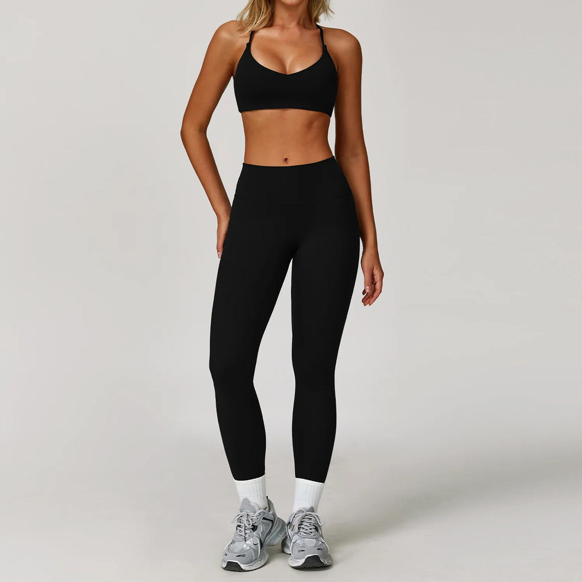 A woman wearing a black three-piece yoga sports set consisting of a sports bra, sports top, and leggings.