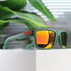 A pair of green polarized square sunglasses resting on a white surface with blurred green foliage in the background.