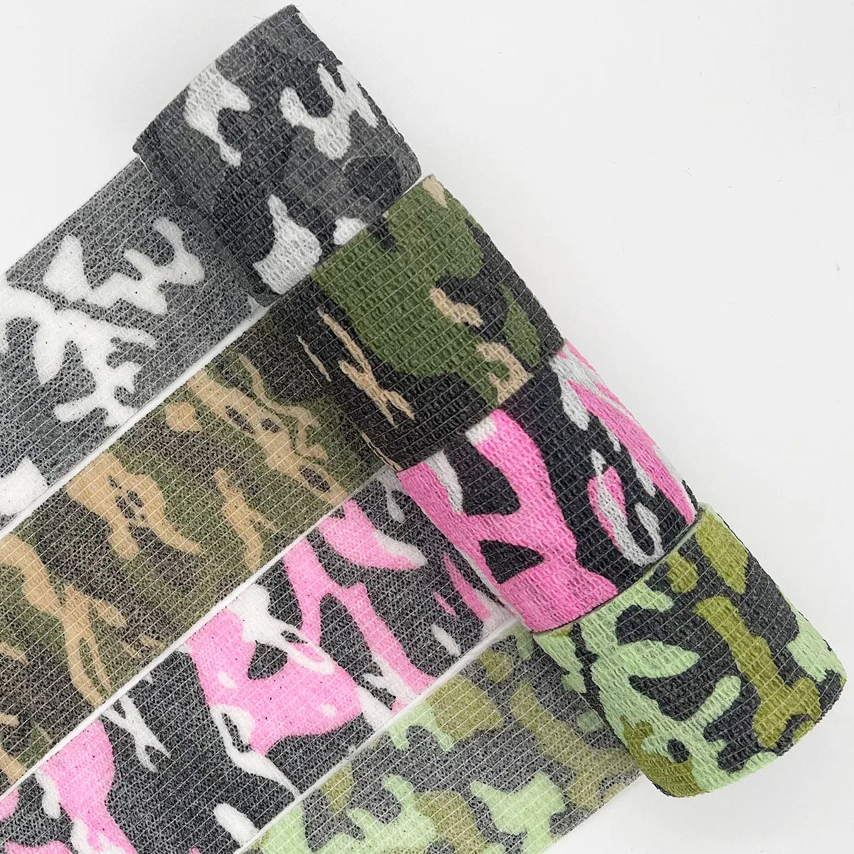 Nahaufnahme mehrerer Rollen selbstklebender Tarngriftape in verschiedenen grün-pinken Mustern.