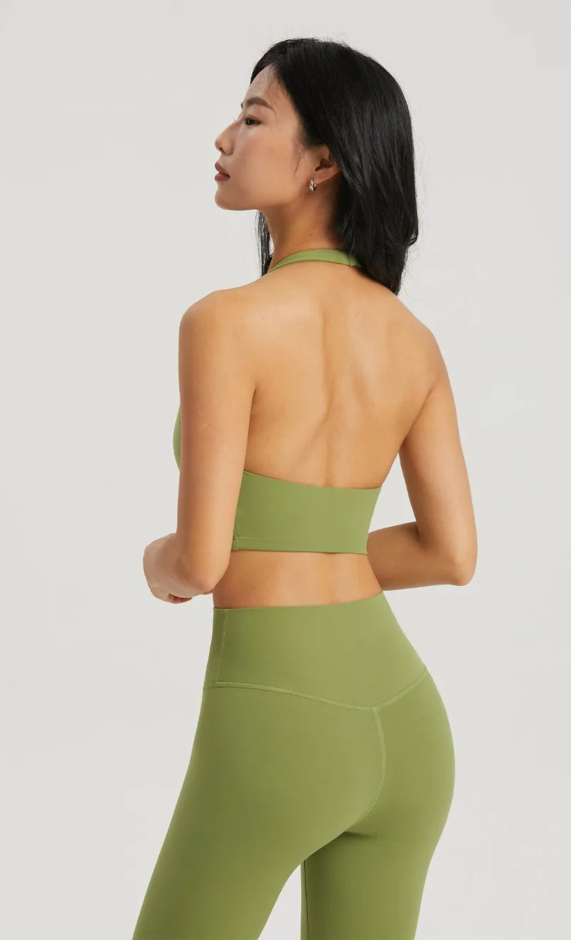 A model wearing a olive green halter neck sports bra top and matching leggings, shown from the back.