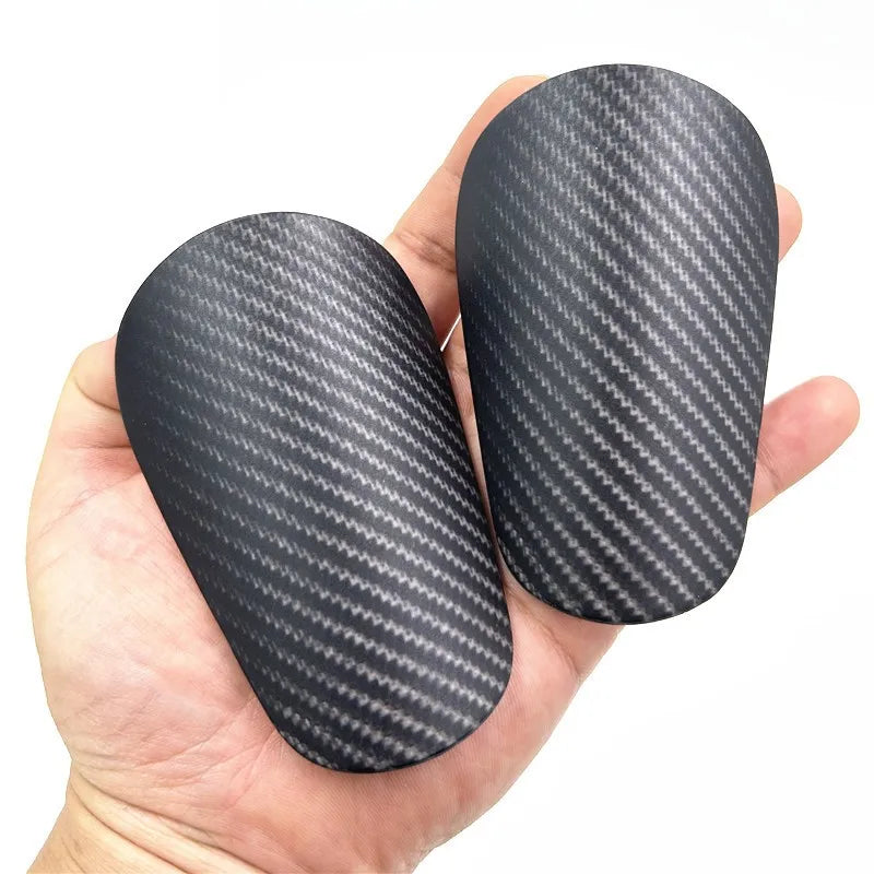 A hand holds a black carbon fiber-look soccer shin guard.