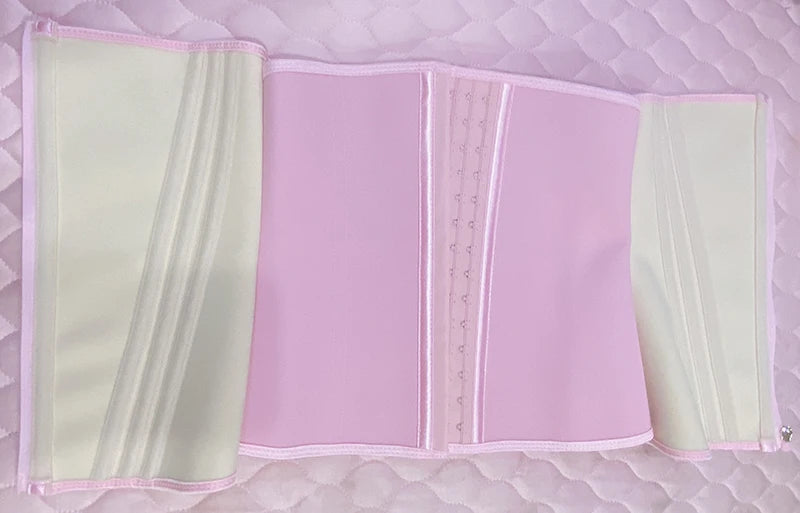 A double compression waist trainer corset body shaper in pink and cream colors displayed on a quilted surface.