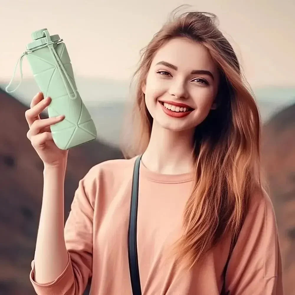 Una mujer joven sostiene una botella de agua de silicona plegable de color verde claro al aire libre.