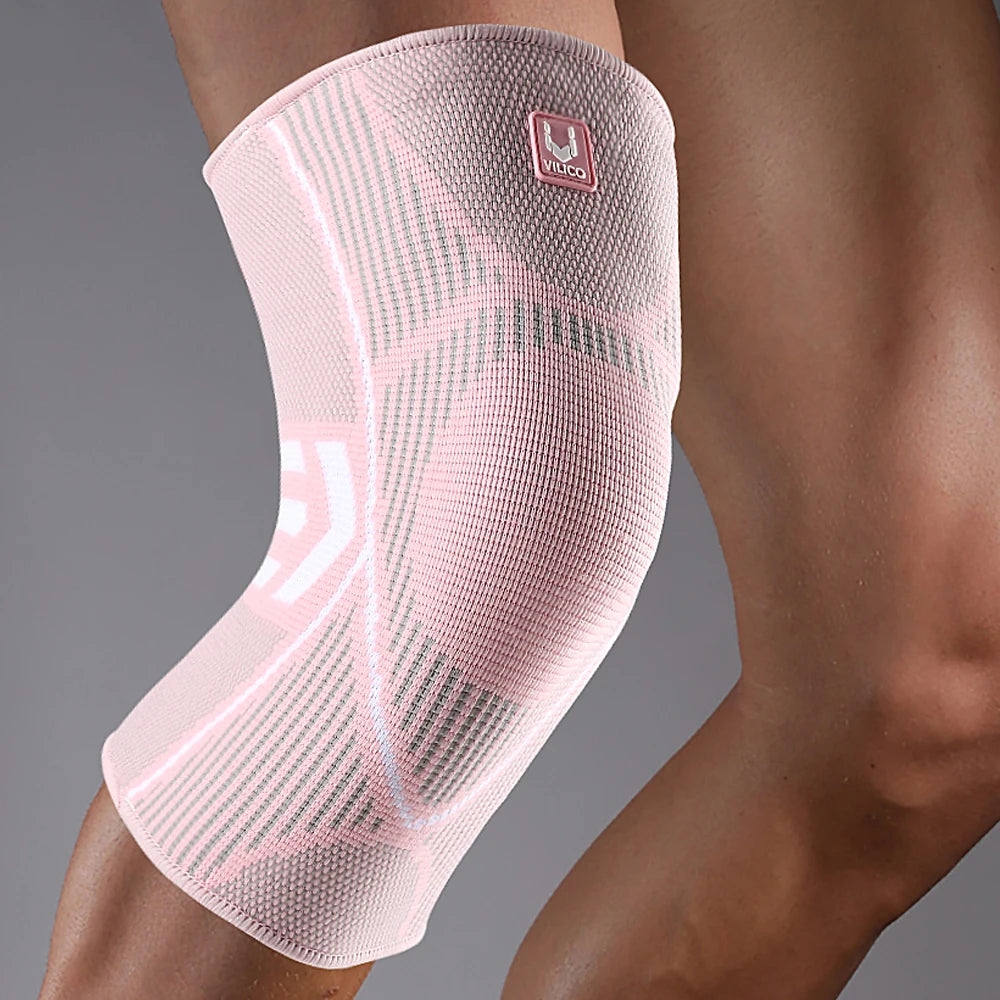 A pink compression knee support sleeve worn on a person's leg.