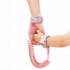 A hand is holding a pink, coiled safety harness and leash for a toddler.