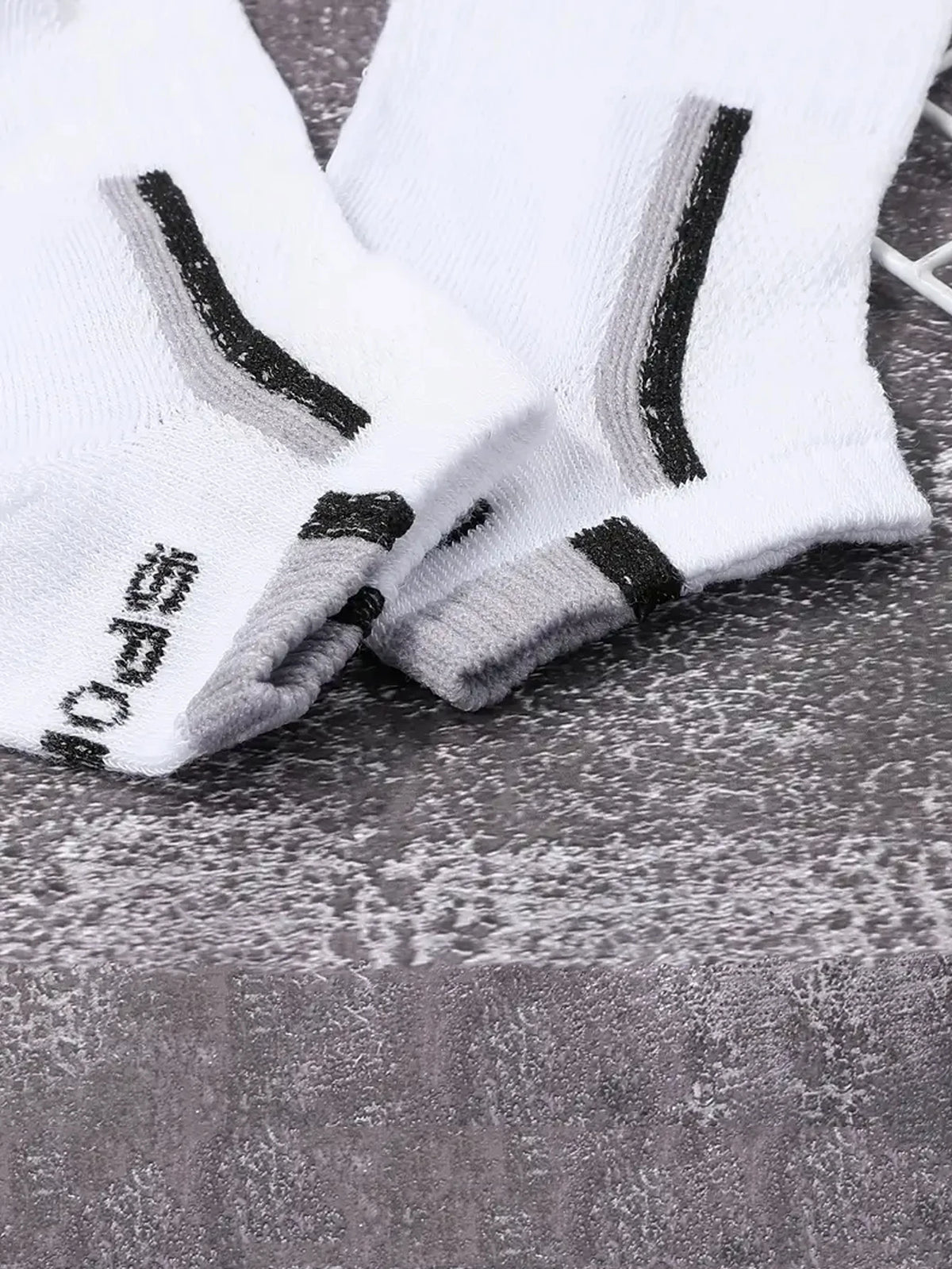 A pair of white and gray color-block mesh ankle socks lying on a dark surface.