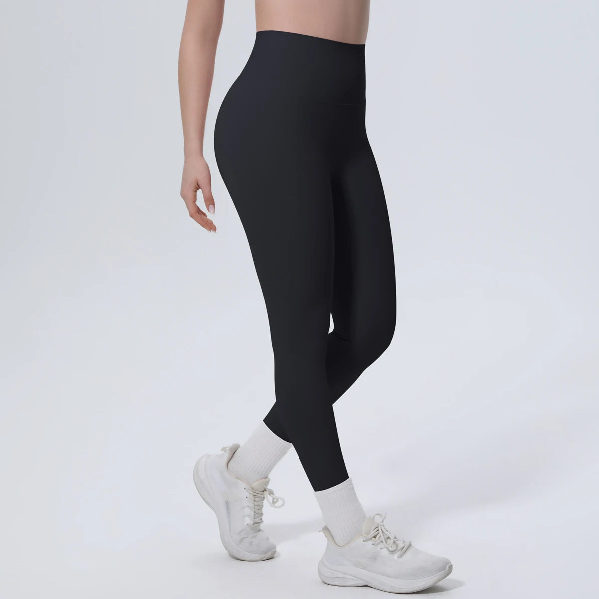A model wearing black high-waisted quick-drying yoga and fitness leggings and white sneakers.