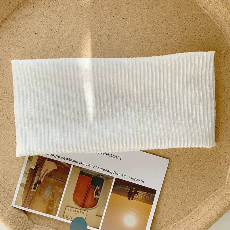 A white, ribbed cotton knitted headband is shown resting on a light brown surface.
