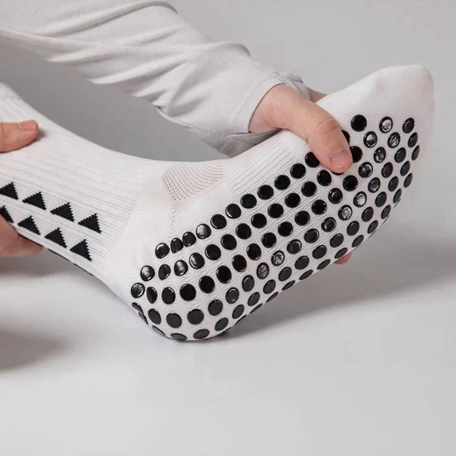 A close-up of white non-slip athletic grip socks being held by a hand, showing the textured grip pattern.
