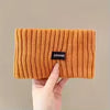 A hand holds an orange knitted headband with the brand name GRANK.