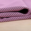 A stack of pink microfiber cooling towels with a black dot pattern resting on a light wooden surface.