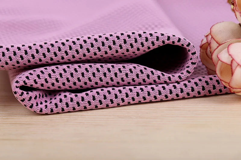 A stack of pink microfiber cooling towels with a black dot pattern resting on a light wooden surface.
