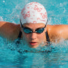 A person wearing a butterfly print silicone swimming cap and goggles is swimming in blue water.