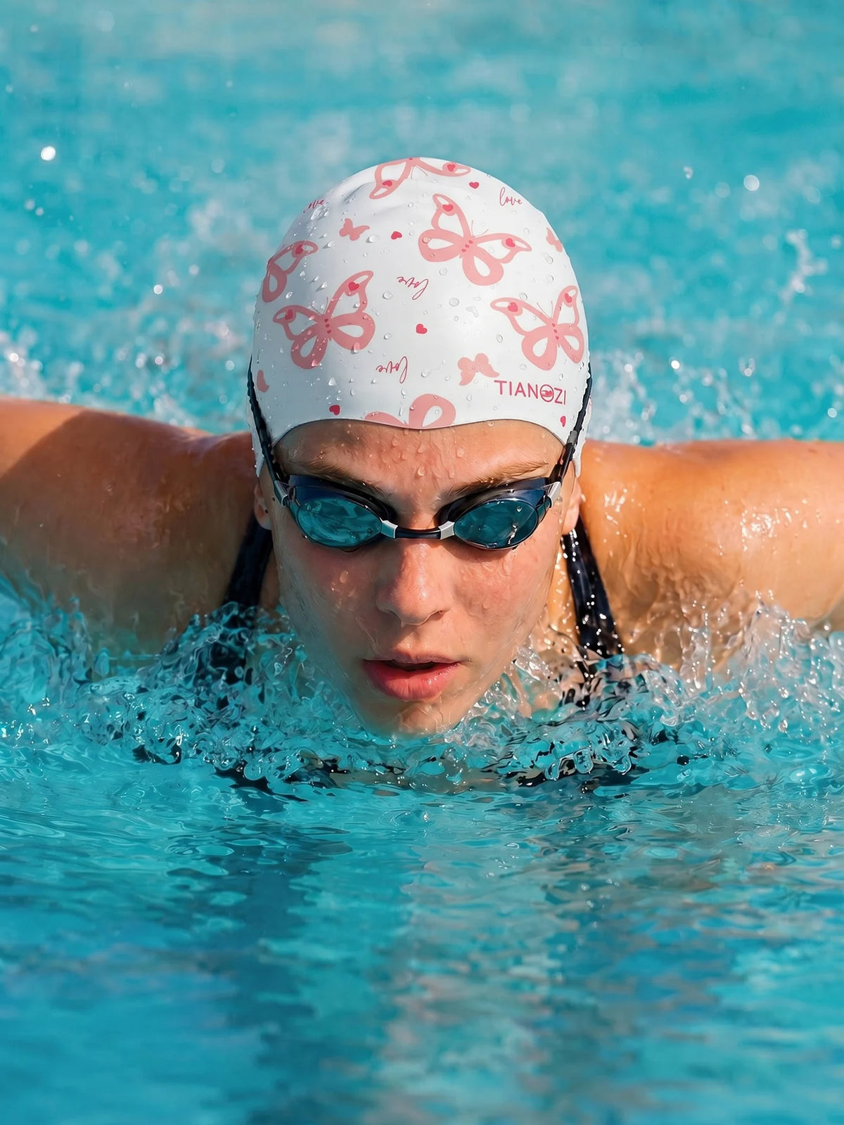 A person wearing a butterfly print silicone swimming cap and goggles is swimming in blue water.