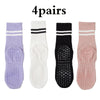 Four pairs of grip socks for yoga and barre exercise in purple, white, black, and pink.