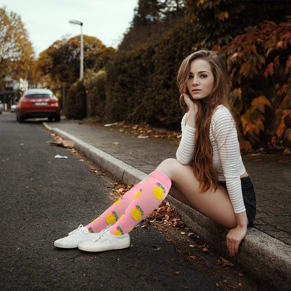 A young woman wearing pink and yellow knee-high compression socks sitting on a curb outdoors.