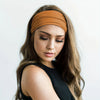 A woman with long brown hair wears a tan elastic headband while looking down.