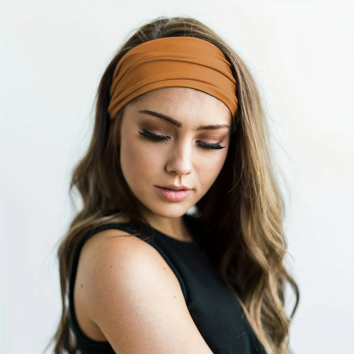 A woman with long brown hair wears a tan elastic headband while looking down.