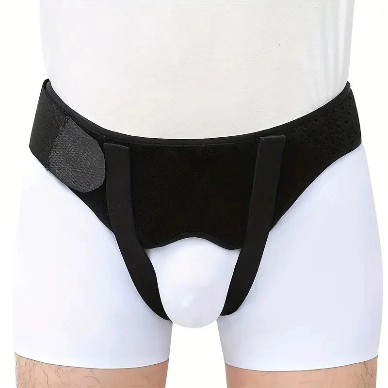 Black hernia support belt worn around the abdomen of a person wearing white shorts.