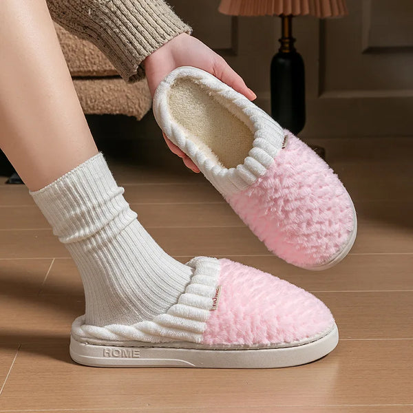 A pair of pink and white plush fleece slippers being held, showing the interior lining and exterior texture.