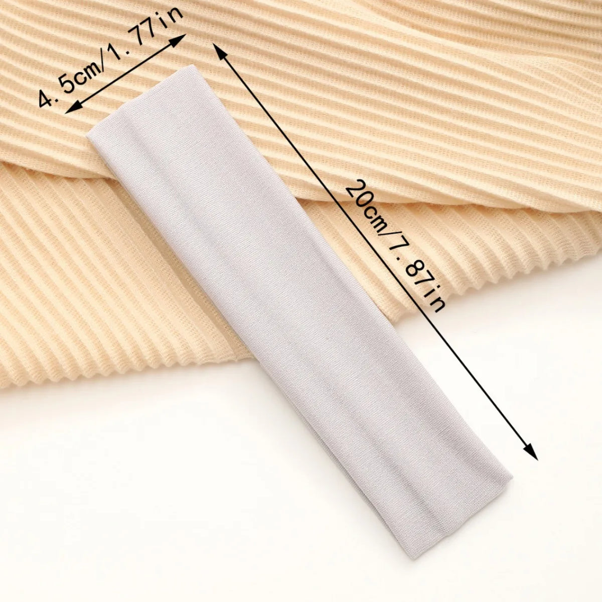 A gray stretchable cotton sweat absorbing headband is shown rolled out on a beige ribbed fabric.