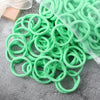 A pile of 50 pieces of mixed color elastic hair bands, some green and some clear, lying on a gray surface.