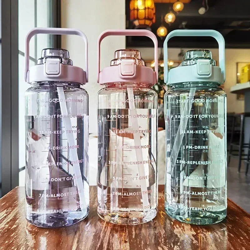 Three clear insulated water bottles with pink and blue lids and time markers sitting on a wooden surface.