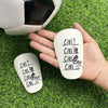 A hand holds a white mini wear-resistant shin guard with handwritten text on its surface, next to a soccer ball on green gras