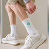 A close-up of a man wearing white sneakers and white crew socks while modeling streetwear apparel.