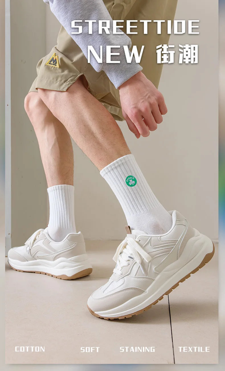 A close-up of a man wearing white sneakers and white crew socks while modeling streetwear apparel.