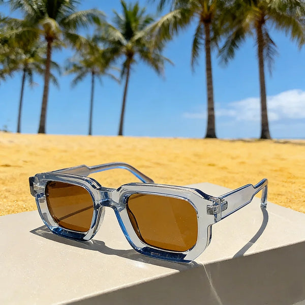 Lunettes de soleil en plastique vintage rectangulaires à verres ambre sur une surface claire avec fond de plage tropicale