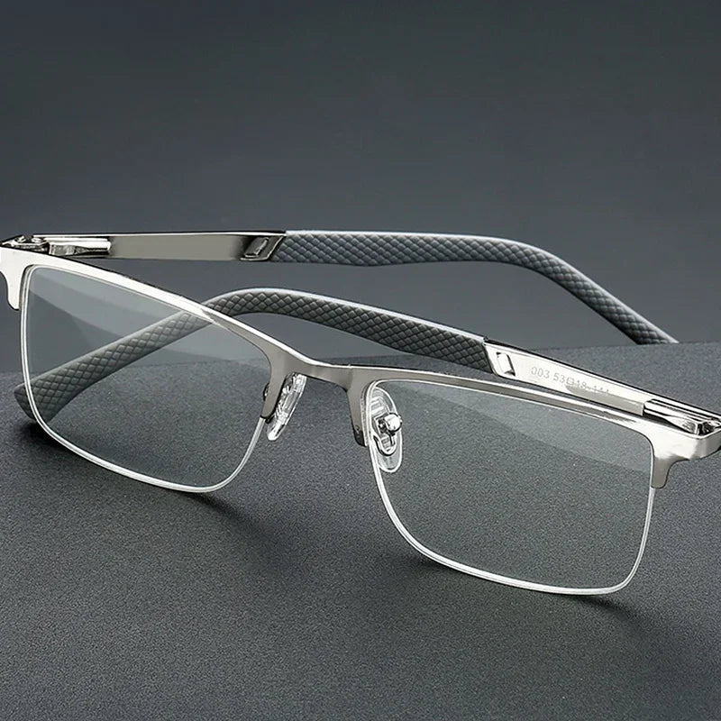 A pair of silver-framed reading glasses with dark gray textured arms and clear lenses resting on a dark surface.