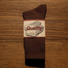 A pair of dark brown tube socks with a white label featuring the word Quality